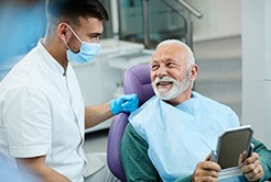 Senior patient looking at dentist while holding small mirror