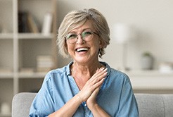 Senior woman with glasses smiling on couch at home