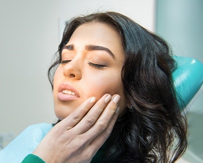Woman in dental chair holding cheek needs emergency dentistry