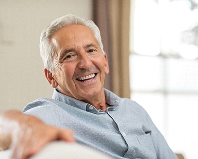 Elderly man smiling and resting his arm over back of couch