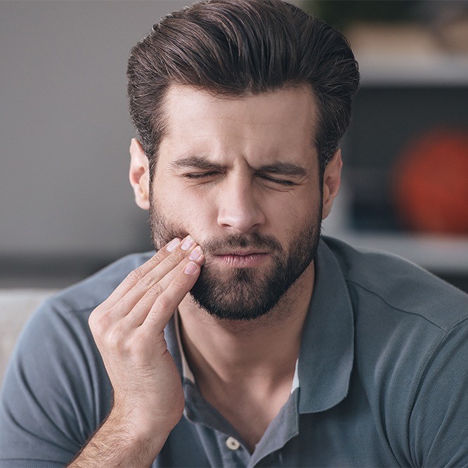 Man holding his cheek in pain before restorative dentistry in Fort Worth