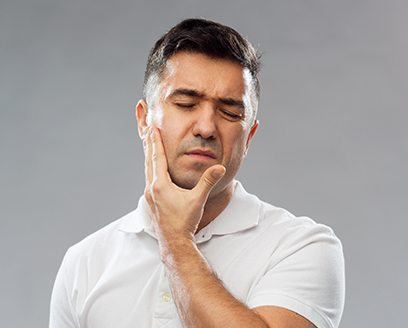 Man in white polo shirt holding his cheek in pain