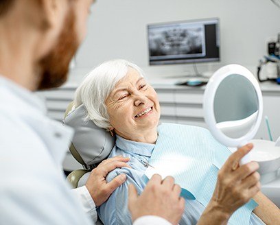 Older woman looking at smile in mirror after full mouth reconstruction