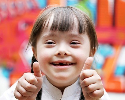 Girl with special needs smiling and giving two thumbs up
