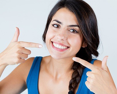 Woman with hair in braid pointing to her smile