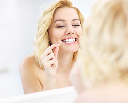 Woman smiling while flossing her teeth in front of mirror