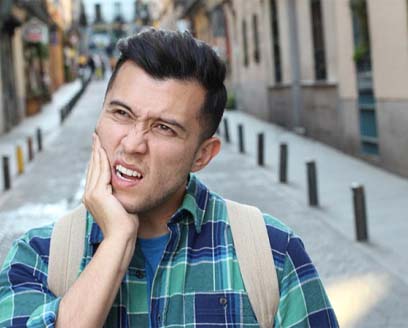 Man on city street holding his cheek in pain