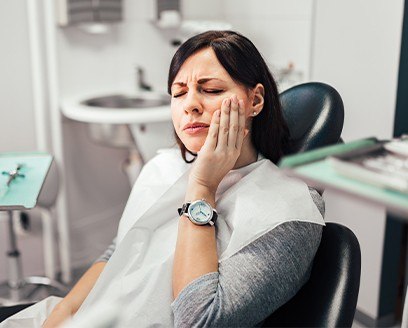 Woman in dental chair holding cheek before tooth extraction