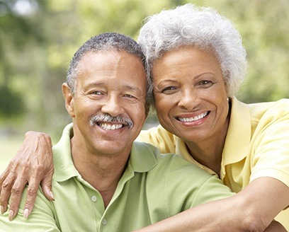 Older man and woman with dental implants smiling outdoors