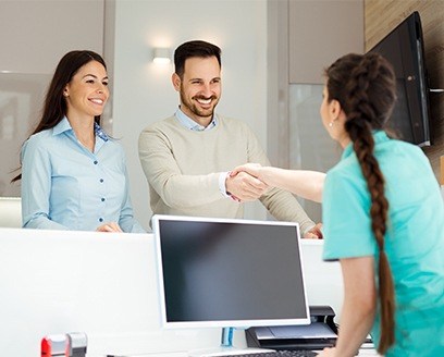 Smiling man and woman checking in at dental office reception desk