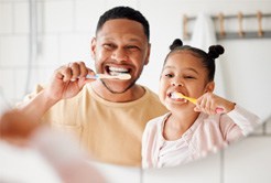 Father and daughter smiling while brushing their teeth
