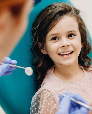 Little girl with brown hair in dental chair about to undergo exam