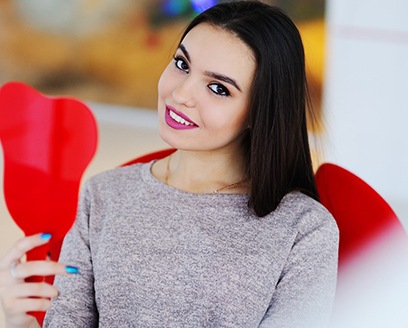 Young woman using mirror to admire the results of her smile makeover