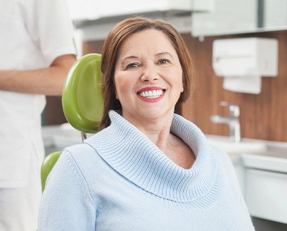 Older woman with denture in dental chair smiling