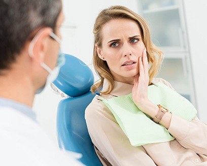 Woman in dental chair holding cheek before root canal