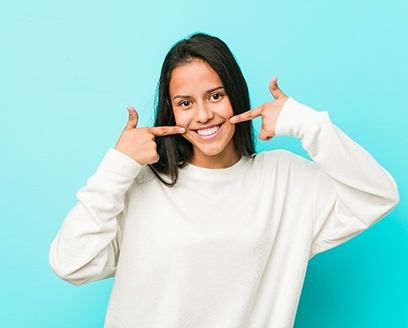 Woman pointing to her smile after teeth whitening in Fort Worth