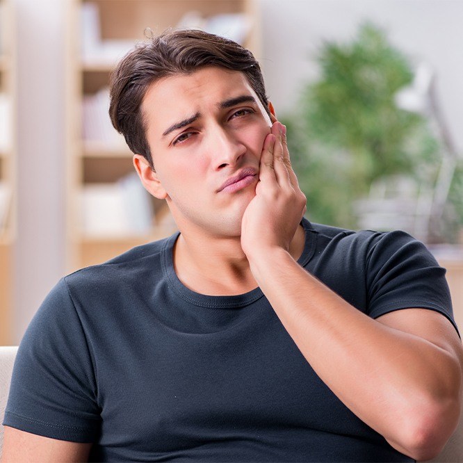 Man in pain holding cheek before wisdom tooth extractions in Fort Worth