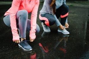 Two women wearing cold weather running gear tying their shoes 