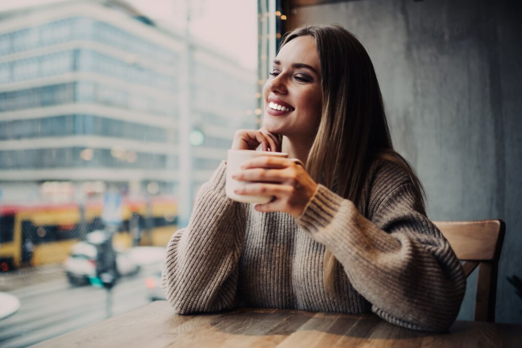 Woman looking out window smiling holding cup of coffee