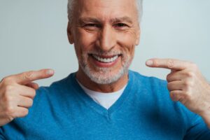 Senior man smiling pointing to dentures.